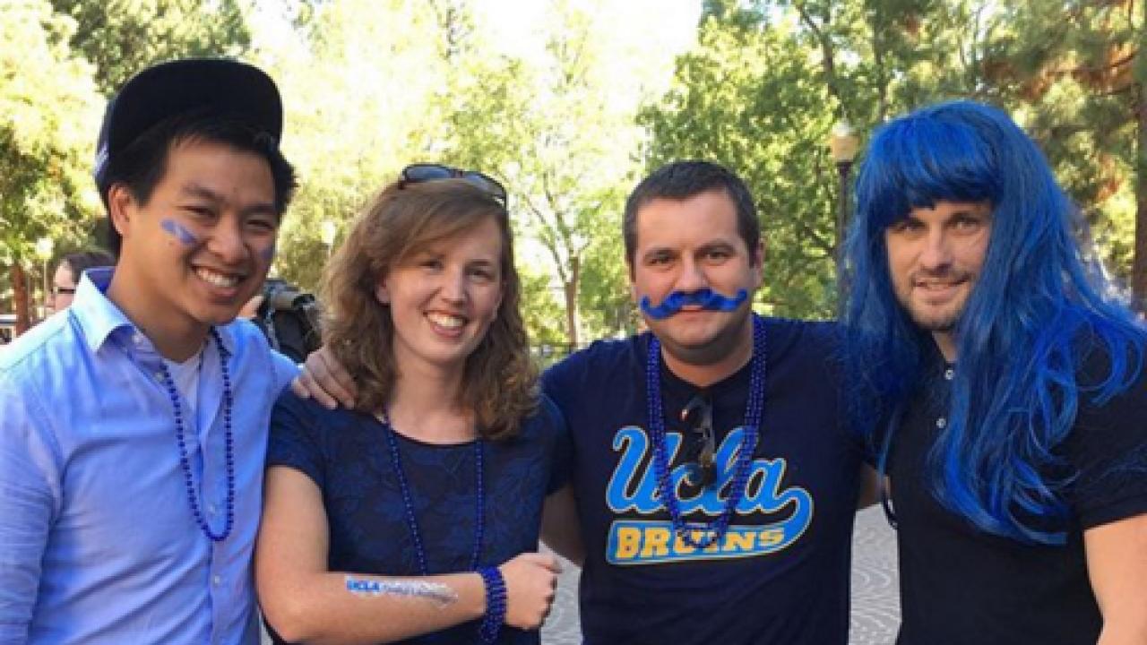 Four people smile and are adorned with blue face paint, wigs, and necklaces.
