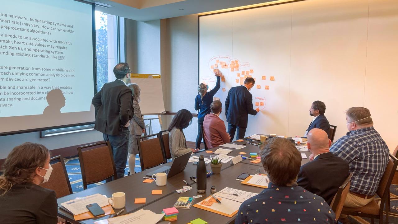 10 academics sit at a conference table and look at a wall filled with sticky-notes.