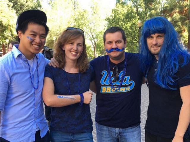 Four people smile and are adorned with blue face paint, wigs, and necklaces.