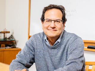 Nelson Freimer, a man with short dark hair and glasses, sits at a university office desk.