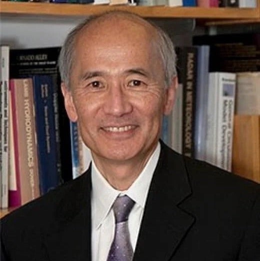 Roger Wakimoto, an East Asian man with silver hair, smiles in front of a bookcase.