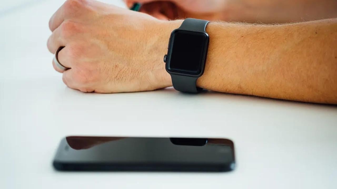 An arm with an Apple Watch lies on a table with an iPhone next to it.