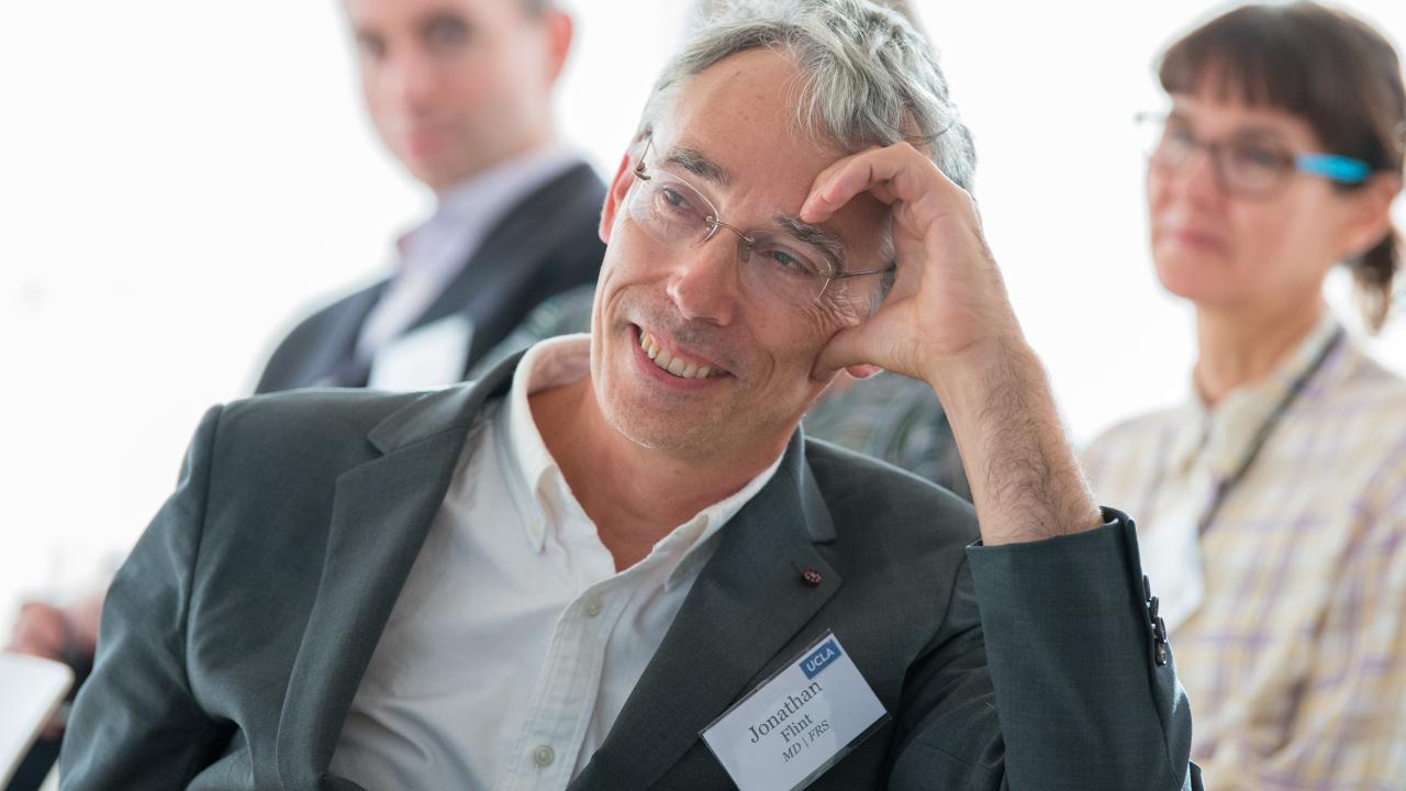 Jonathan Flint, smiling, leaning his head on his hand. He has a light skin tone, silver hair, and glasses.