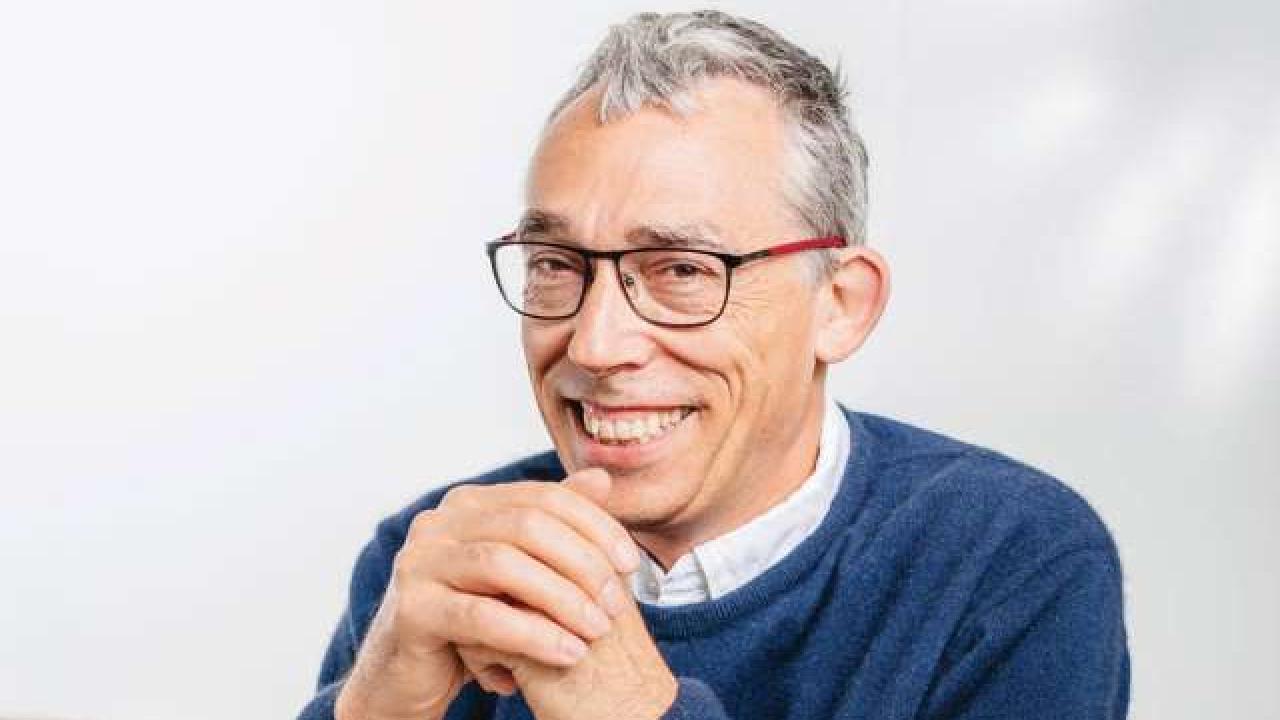 Jonathan Flint smiling. He has light skin, white hair, glasses, and sweater.