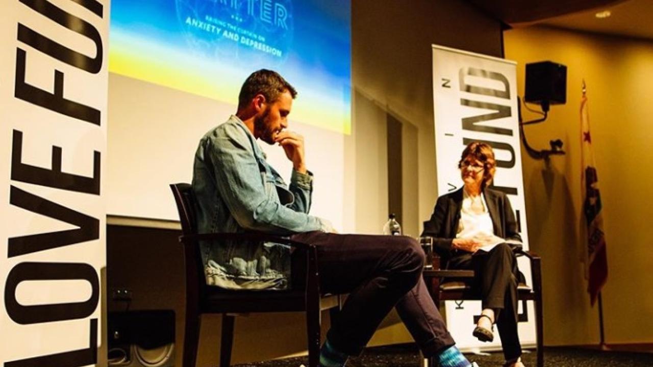 Kevin Love and Michelle Craske seated on a stage. Background signage reads "Love Fund" and "Minds Matter"