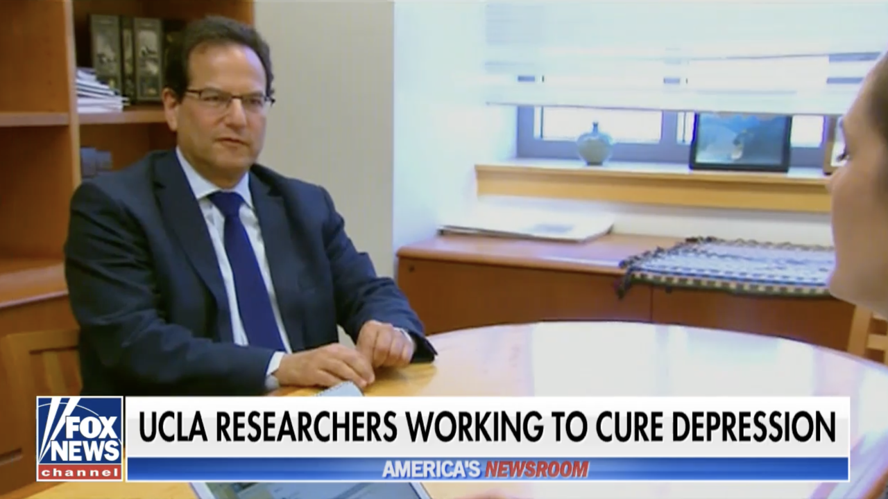 A man in a suit at a table being interviewed. A chryon below reads "UCLA researchers working to cure depression"