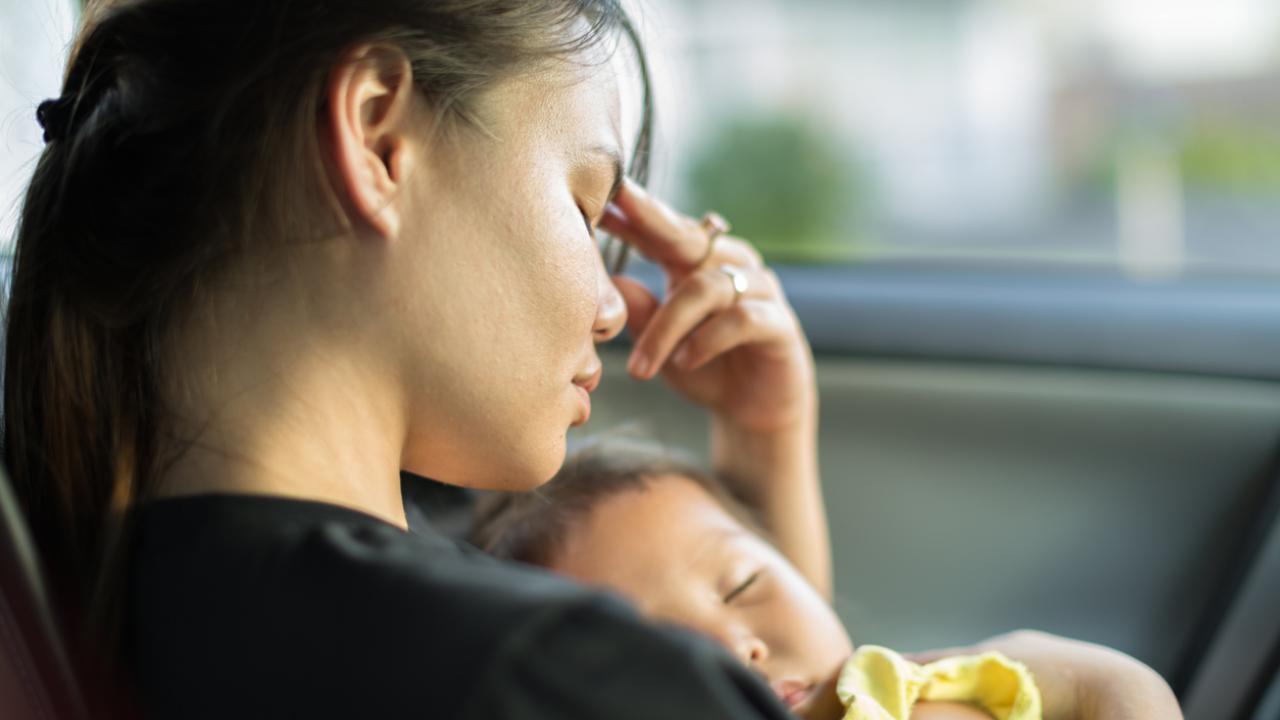 A mother holds a baby to her chest, and looks forlorn with her hand on her forehead.